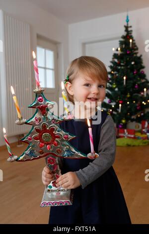 Ragazza di fronte di albero di natale azienda ornamento di Natale guardando sorridente della fotocamera Foto Stock