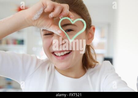 Ragazza cerca attraverso a forma di cuore ad formina sorridente Foto Stock