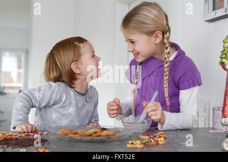 Le ragazze al bancone cucina decorare i cookie faccia a faccia sorridente Foto Stock