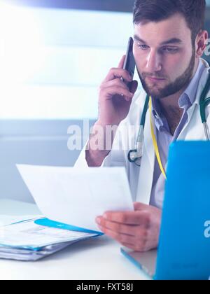 Junior medico utilizza lo smartphone durante la lettura record medici in clinica Foto Stock