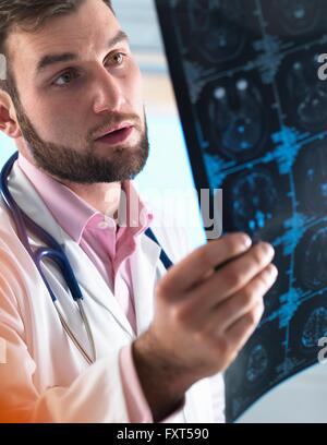 Giovane maschio junior medico esaminando una scansione cerebrale in ospedale Foto Stock