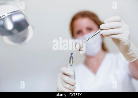 Basso angolo vista del dentista indossando maschera e guanti protettivi azienda apparecchiature odontoiatriche e specchio dentale Foto Stock