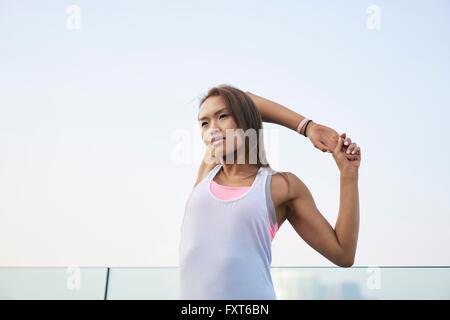 Giovane donna in fase di riscaldamento e di bracci di estensione in città Foto Stock