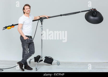 A piena lunghezza Ritratto di un felice fotografo maschio preparazione di apparecchi di illuminazione in studio Foto Stock