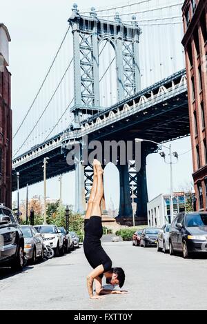 Giovane uomo fare yoga handstand nella parte anteriore del ponte di Manhattan, New York, Stati Uniti d'America Foto Stock