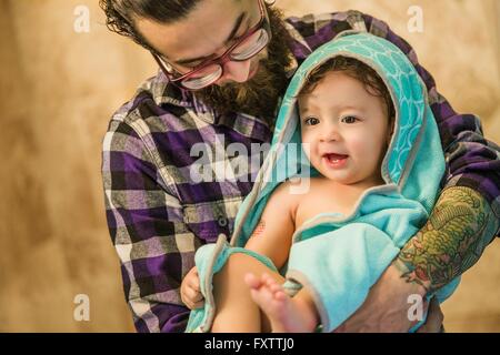 Giovane uomo bambino portando figlio avvolto in asciugamano Foto Stock