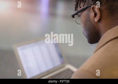 Sulla spalla vista del giovane imprenditore seduto in treno stazione utilizzando laptop Foto Stock