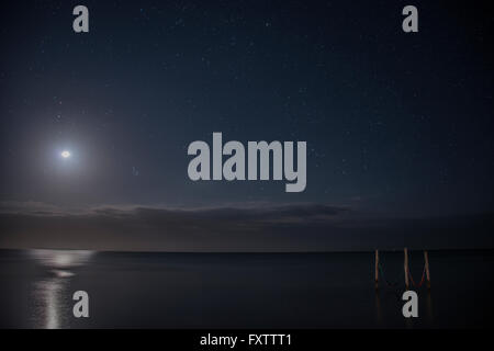 Cielo stellato e luna piena illumina iconico amache sulle acque, Isla Holbox, Messico Foto Stock