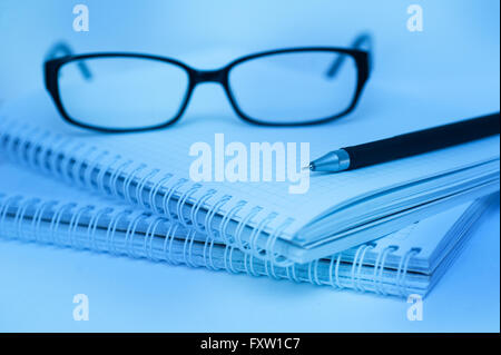 La penna nera e bicchieri giacente su notebook di close-up di colore blu Foto Stock