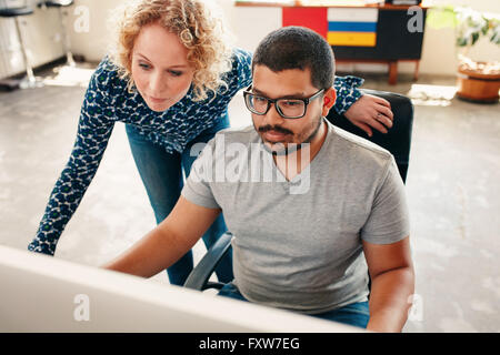 Ritratto di due giovani graphic designer che lavorano su computer in ufficio. Maschio e donna designer guardando il monitor del computer. Foto Stock