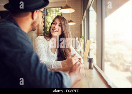 Sorridente giovane donna seduta in un caffè e a parlare con il suo fidanzato. Coppia giovane di trascorrere del tempo presso la caffetteria. Foto Stock