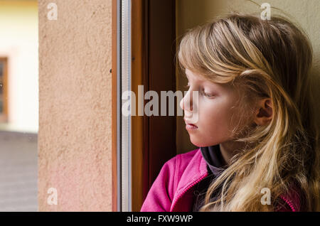 Piccola ragazza guardando attraverso la finestra Foto Stock