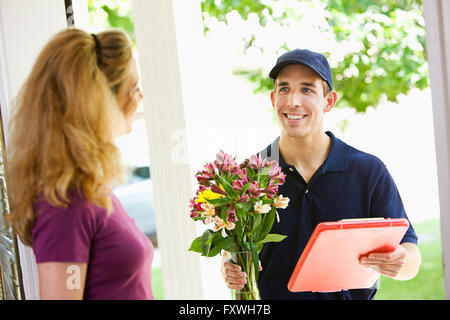 Serie a con un uomo di consegna caduta fiori, scatole, palloncini, ecc per un residenziale casa suburbana. Foto Stock