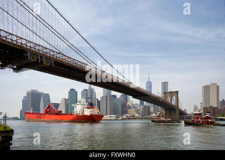 Nave da carico e rimorchiatore sotto il ponte di Brooklyn, New York City Foto Stock