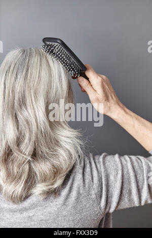 Vista posteriore della donna la spazzolatura lungo i capelli grigi Foto Stock