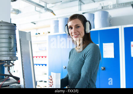 Donna in officina di indossare le cuffie di protezione guardando sorridente della fotocamera Foto Stock