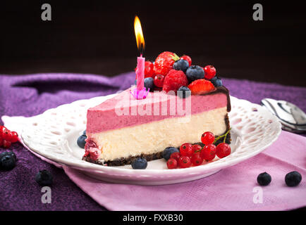 Porzione di deliziosa Cheesecake ai lamponi e decorate con frutti di bosco freschi, cioccolato e candela Foto Stock