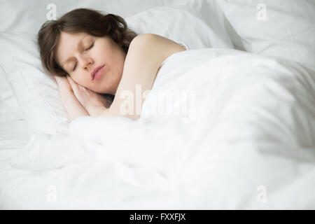 Ritratto di giovane donna che dorme nel letto. Modello femminile rilassante la mattina a casa sotto la calda coperta Foto Stock