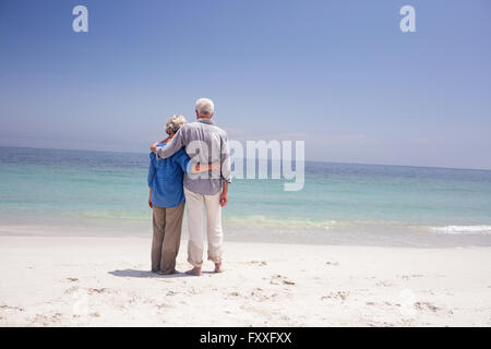 Vista posteriore della coppia senior che abbraccia ogni altro sulla spiaggia Foto Stock