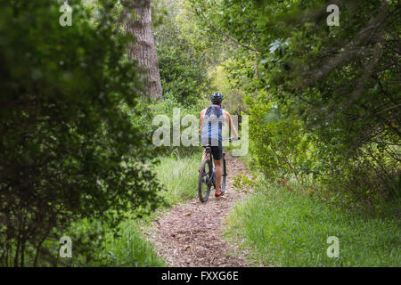 Vista posteriore dell'uomo equitazione bicicletta su strada sterrata Foto Stock