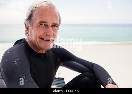 Ritratto di felice uomo senior in wetsuit seduto sulla spiaggia Foto Stock