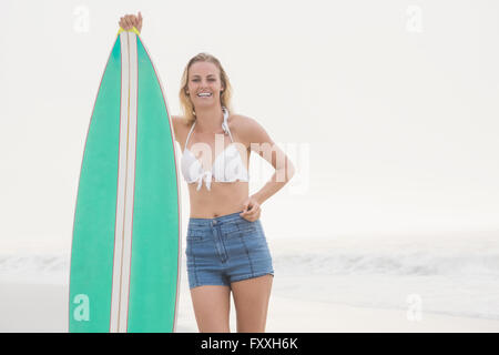 Bella donna bionda in piedi accanto ad una tavola da surf Foto Stock