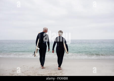 Vista posteriore della coppia senior in muta in possesso di una tavola da surf Foto Stock