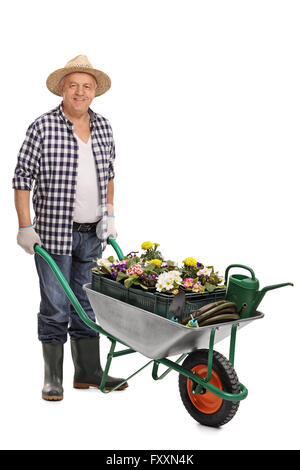 A piena lunghezza Ritratto di un uomo maturo spingendo una carriola piena di attrezzature da giardinaggio e fiori isolati su sfondo bianco Foto Stock