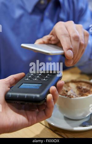 Uomo che utilizza il pagamento senza contatto App sul telefono cellulare in Cafe Foto Stock