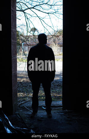 Silhouette di un uomo in piedi nel vano della porta di un edificio abbandonato Foto Stock