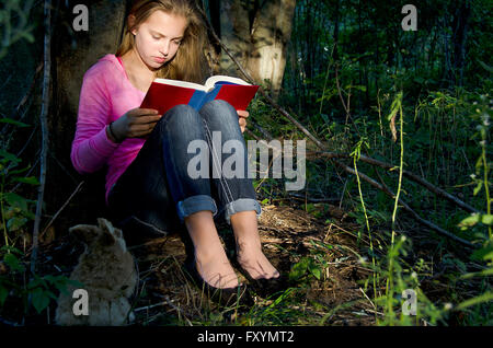 Ragazza giovane leggendo un libro nella luce del sole nella foresta con coniglio. Foto Stock