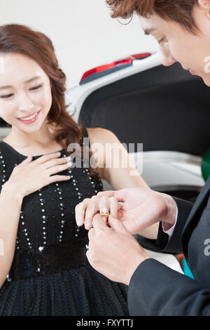 Ritratto di giovane uomo propone di giovane donna sorridente mettendo un anello sul suo dito Foto Stock