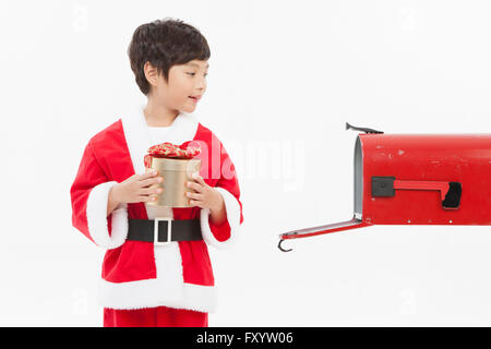 Ritratto di ragazzo sorridente in santa gli abiti tenendo un presente box cercando di aprire la casella di posta Foto Stock