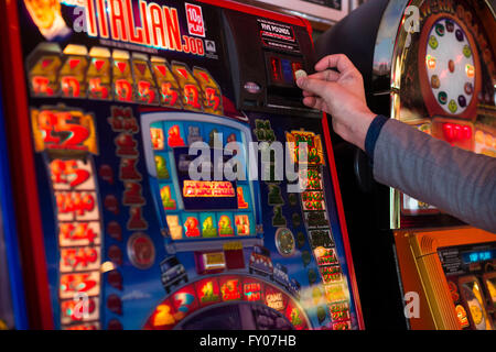 Una mano d'uomo mettere soldi in una macchina di frutta il gioco d'azzardo Foto Stock