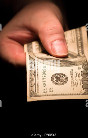 Un uomo della mano destra emergendo dalle ombre tenendo fuori un $100 bill Foto Stock