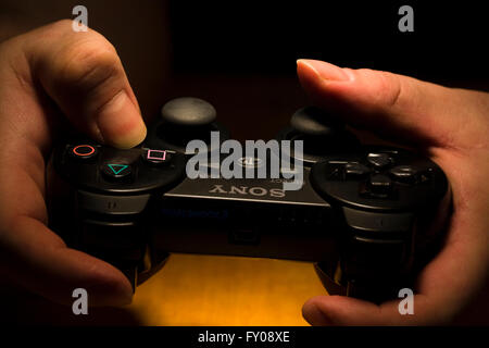 Due mani tenendo un wireless Sony Playstation Dual Shock 3 Controller mentre il pollice si manipolano i pulsanti Foto Stock