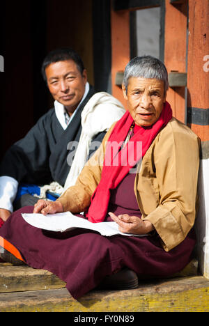 Anziani Vajrayana monaca buddista in veste di cremisi e uomo bhutanesi nei tradizionali gho seduti sulla terrazza a paro Dzong, Bhutan Foto Stock