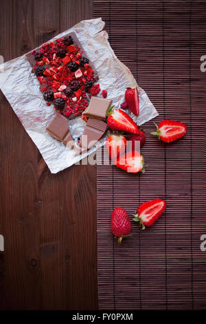 Cioccolato artigianale con freschi e frutta secca, lamponi, fragole, ribes, more, il cacao in polvere su sfondo in legno in stile rustico Foto Stock