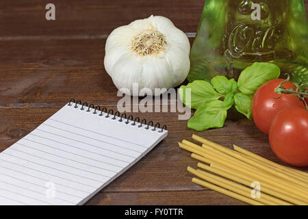 Blank notebook con carta rigata, aglio, foglie di basilico, spaghetti, olio d'oliva in una bottiglia e i pomodori sono giacenti sul tavolo Foto Stock