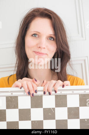 Donna sorridente tenendo la scacchiera in home interni. Concetto di strategia, attività di svago e di giochi. Foto Stock