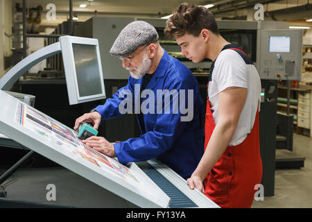 Giovane lavoratore guardando coppia collega facendo controllare la qualità di stampa con lo scanner Foto Stock