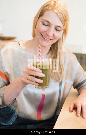 Felice donna matura tenendo un frappè in un bicchiere a casa Foto Stock