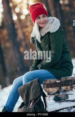 Giovane donna che guarda lontano mentre è seduto sul log durante il periodo invernale Foto Stock