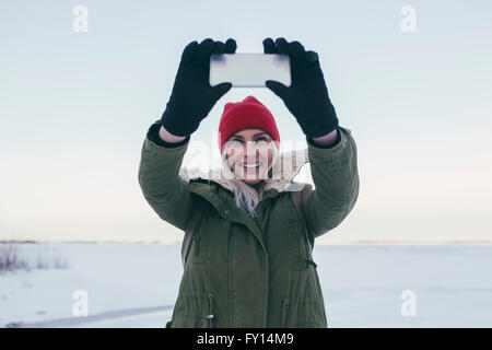 Giovane donna prendendo selfie su smart phone durante il periodo invernale Foto Stock
