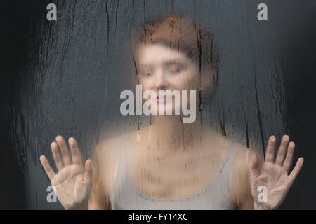 Premurosa donna in piedi di fronte sul vetro condensato su sfondo nero Foto Stock