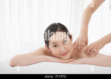 Ritratto di giovane donna sorridente getting massaggio della spalla fissando sulla parte anteriore Foto Stock