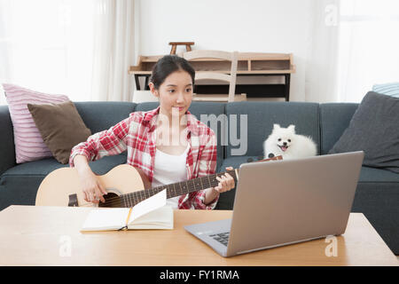 Ritratto di giovane donna con il suo cucciolo di suonare una chitarra utilizzando computer notebook Foto Stock