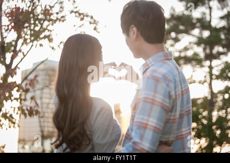 Ritratto di giovane coppia costituente un cuore insieme contro il sole Foto Stock