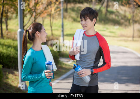 Vista laterale Ritratto di giovane coppia sorridente in sportswears faccia a faccia con bottiglie d'acqua e asciugamani Foto Stock