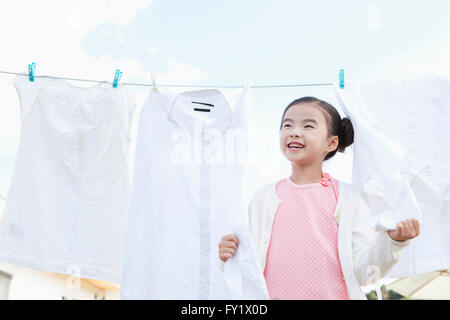 Ragazza con un servizio lavanderia appeso su una linea fuori e sorridente Foto Stock